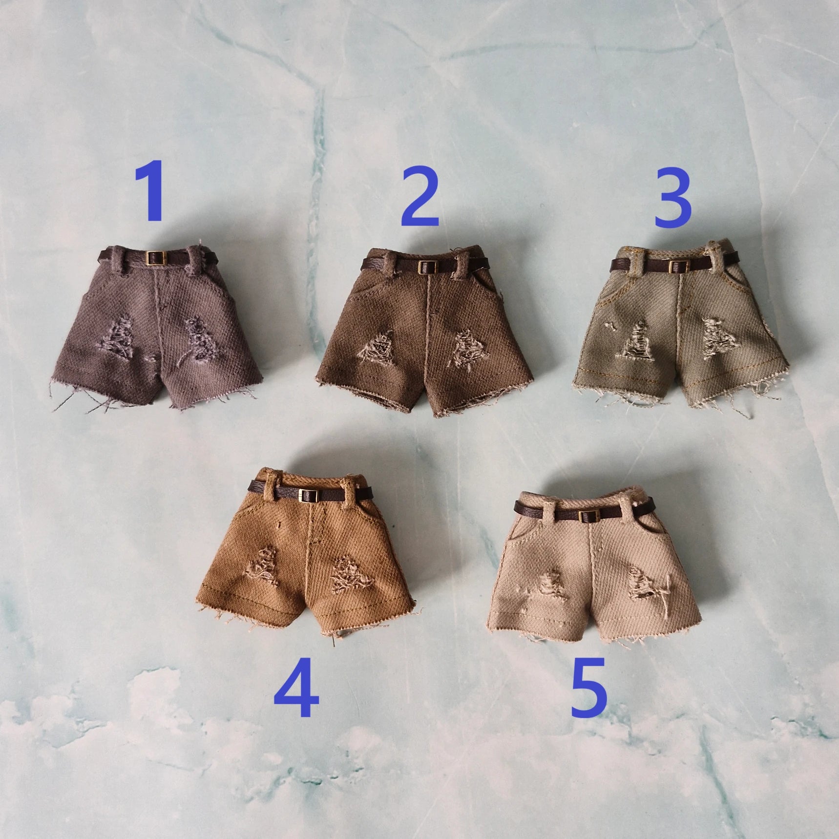 Five pairs of distressed denim shorts with varying shades on a textured gray background.