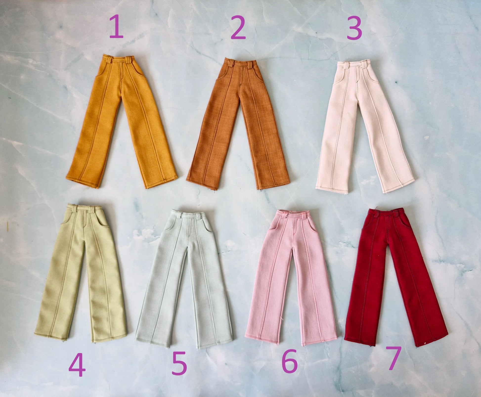 Flat lay of seven different colors of wide-leg Barbie doll pants numbered one through seven