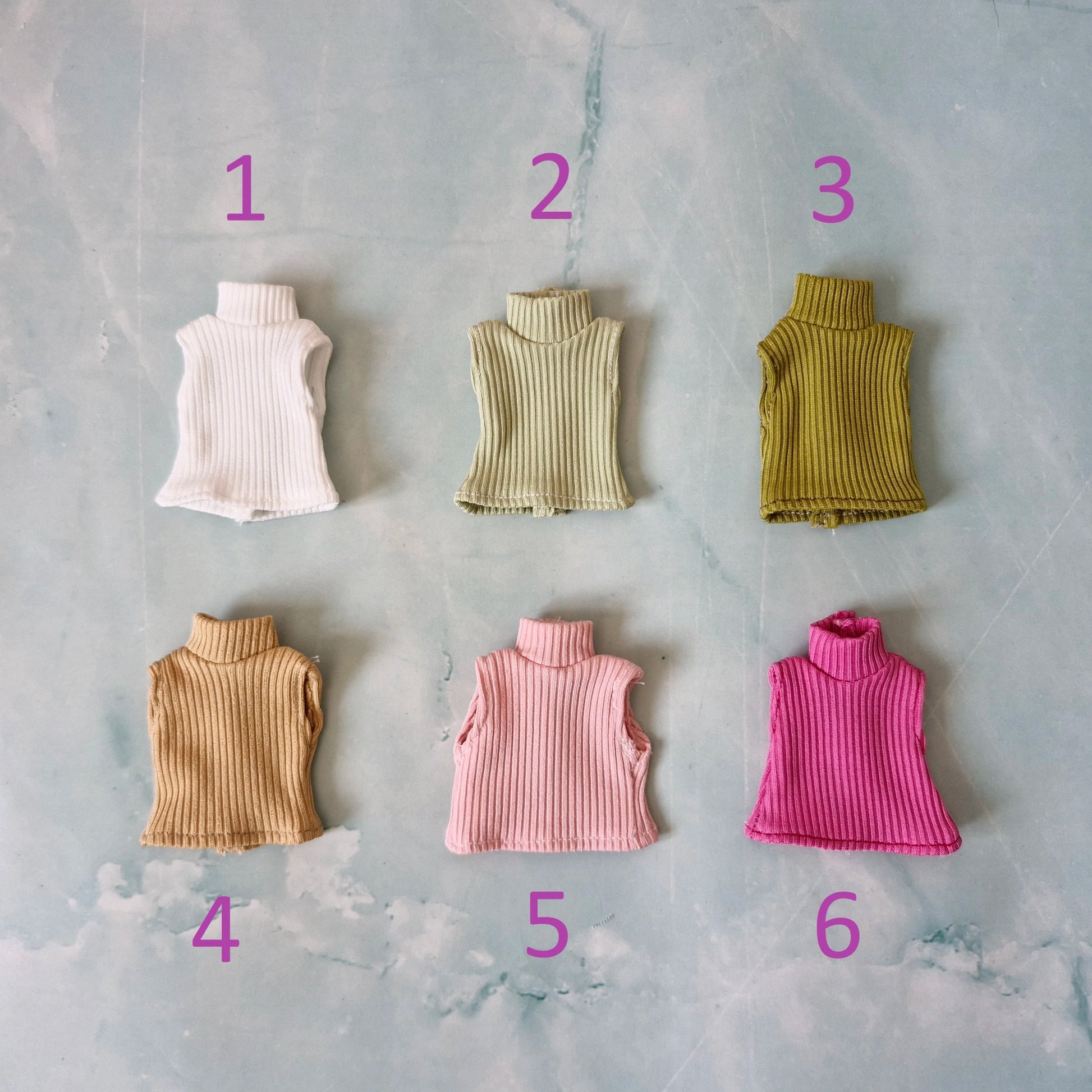 Flat lay of six different colors of ribbed sleeveless Barbie doll tops numbered one through six