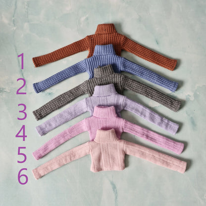 Set of six knitted sweater tops in different colors on a textured surface.