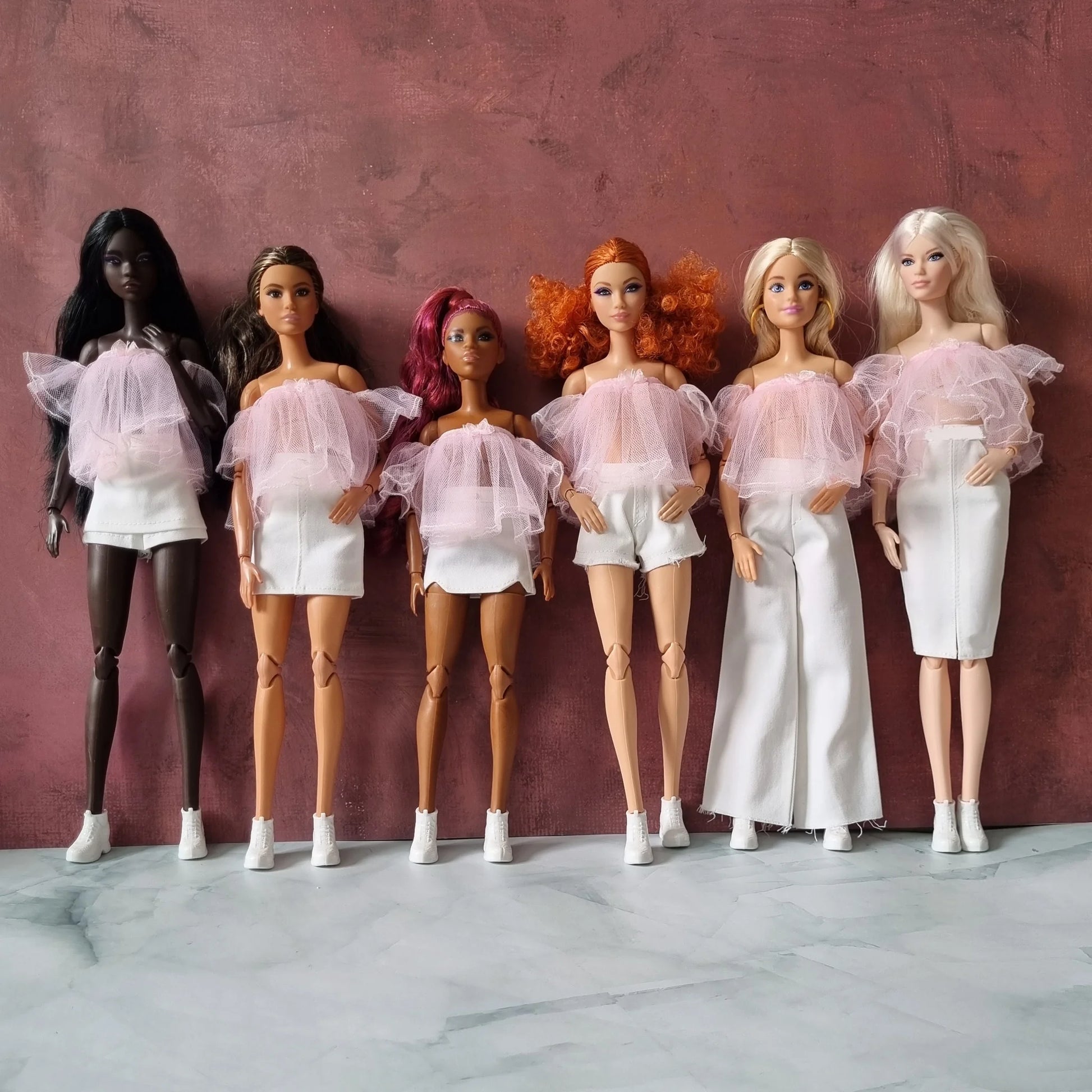 Fashion dolls wearing matching pastel pink tulle tops and white skirts, shorts, and pants – chic doll outfit collection for online shop